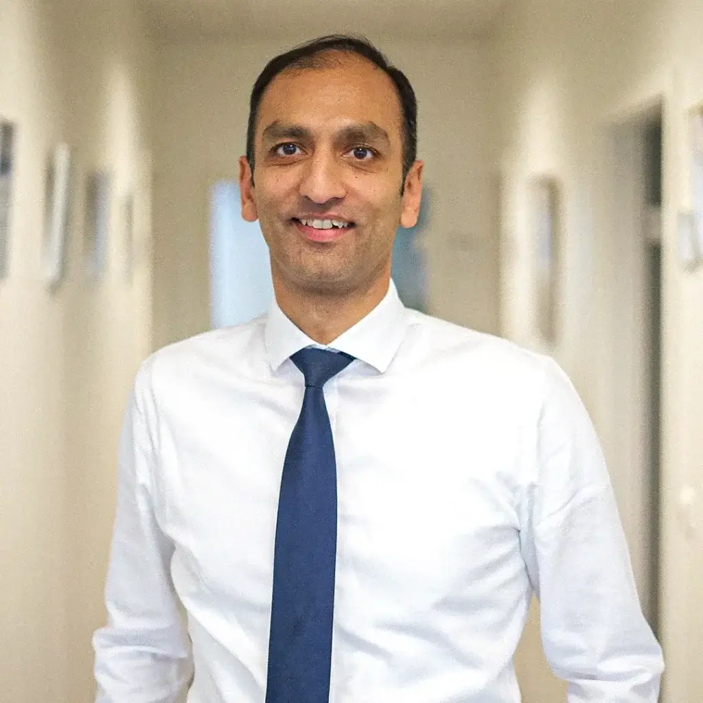 Rehan Khan lächelt in die Kamera. Ein Büroflur ist im Hintergrund.